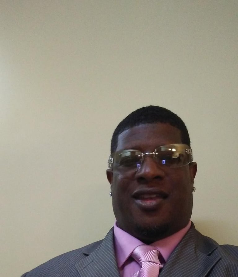 Portrait of a smiling man wearing glasses, gray blazer, and pink dress shirt